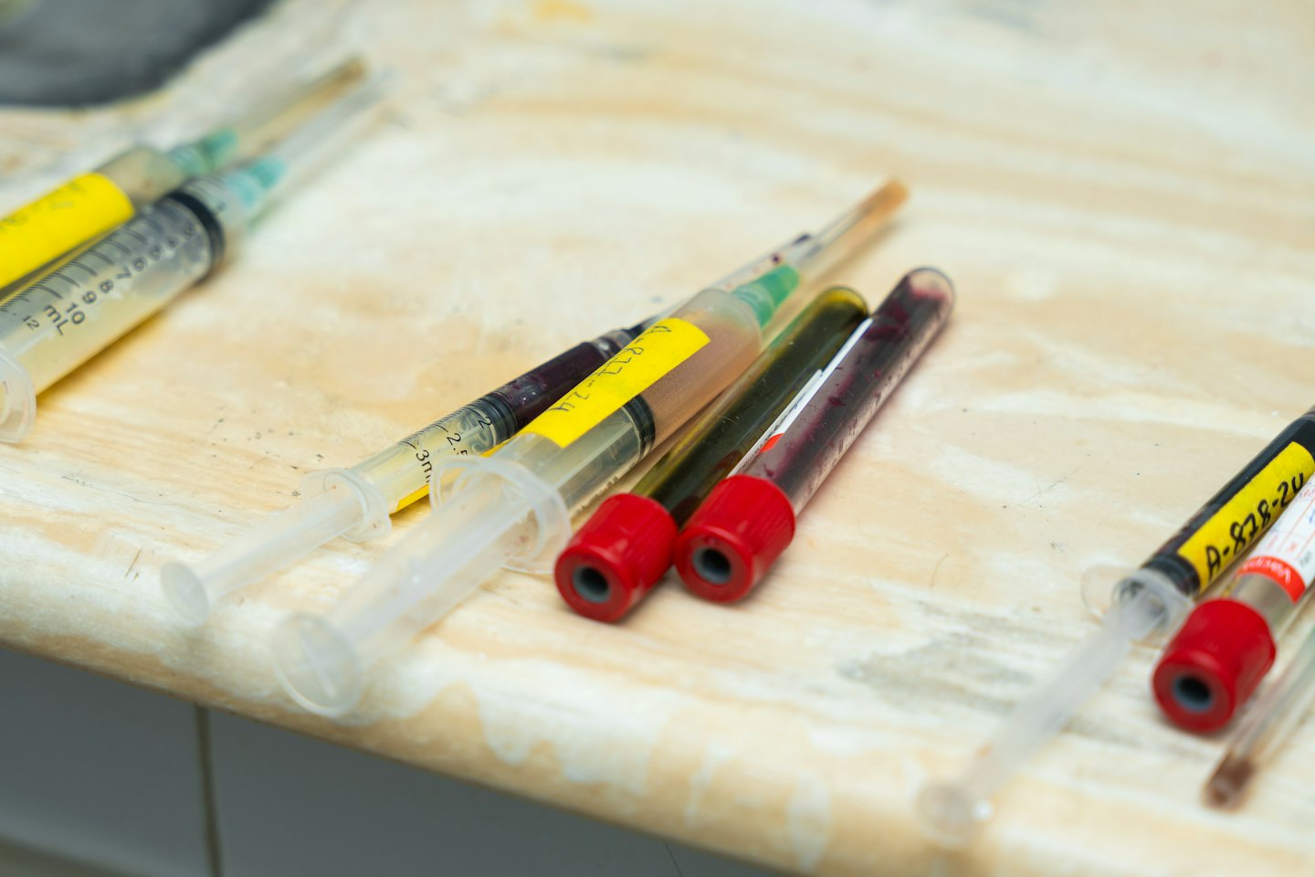 Medical syringes and test tubes with samples on a countertop.
